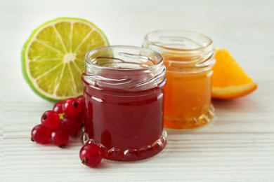 Photo of Jars of sweet red currant and citrus jams on white wooden table