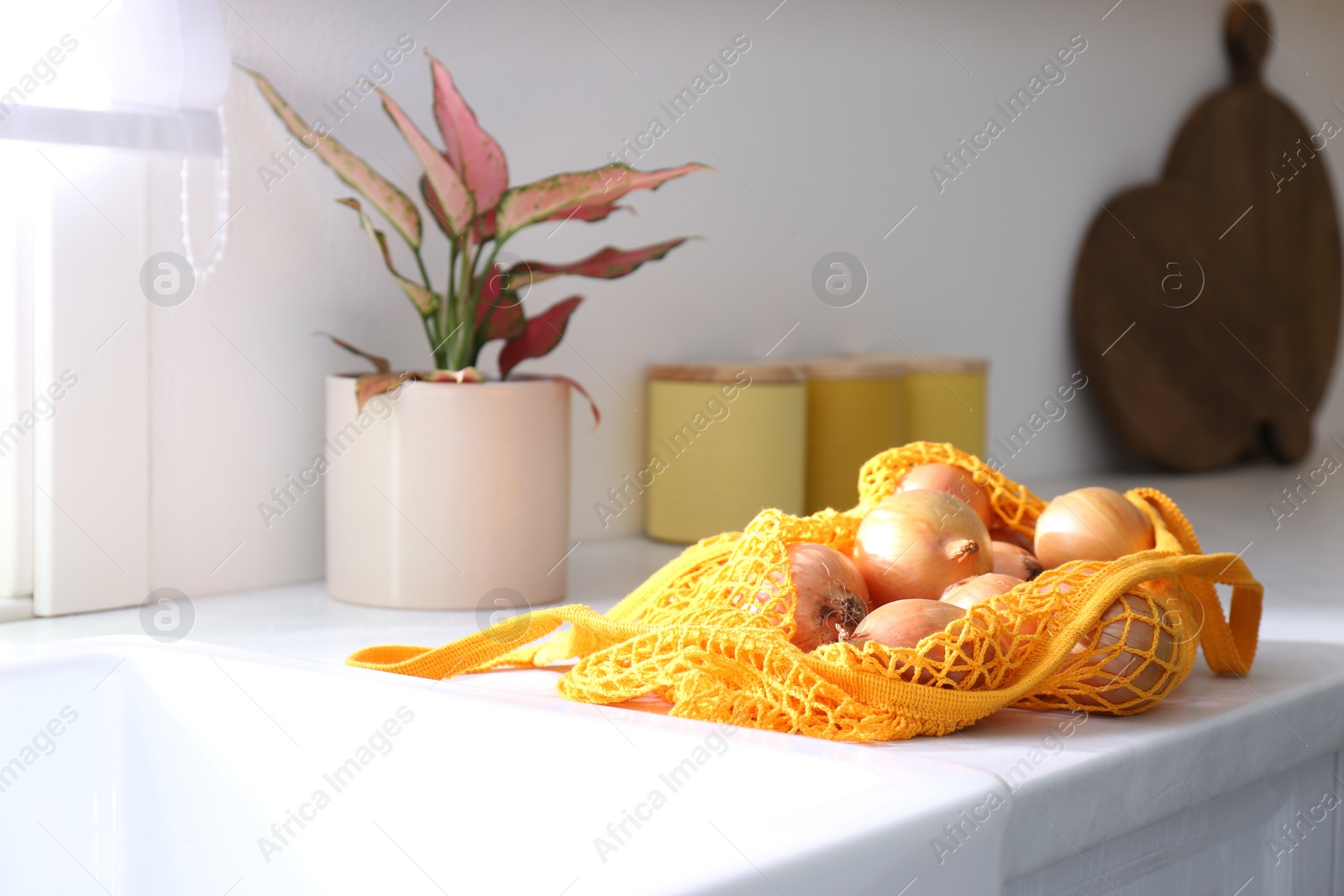 Photo of Golden onions in mesh tote bag on countertop of kitchen