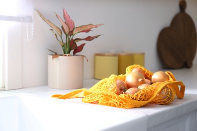 Photo of Golden onions in mesh tote bag on countertop of kitchen