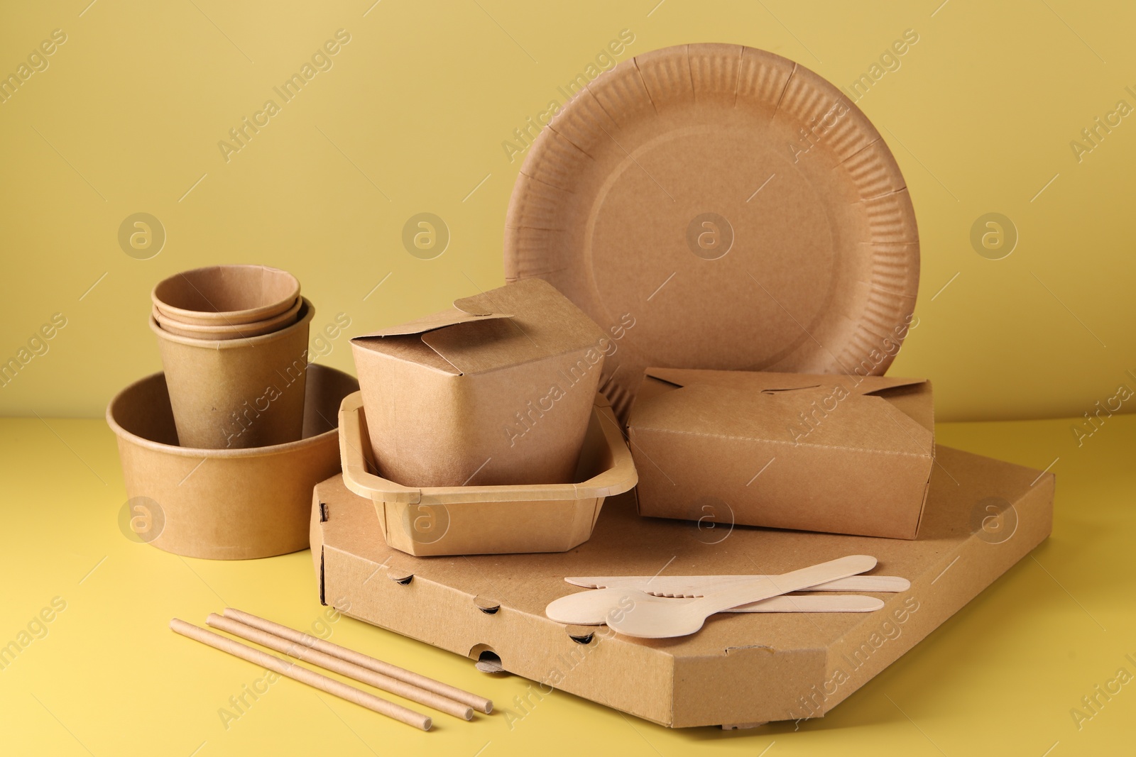 Photo of Eco friendly food packaging. Paper containers and tableware on pale yellow background