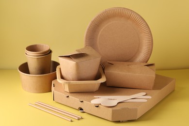 Photo of Eco friendly food packaging. Paper containers and tableware on pale yellow background