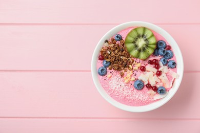 Photo of Tasty smoothie bowl with fresh kiwi fruit, berries and granola on pink wooden table, top view. Space for text