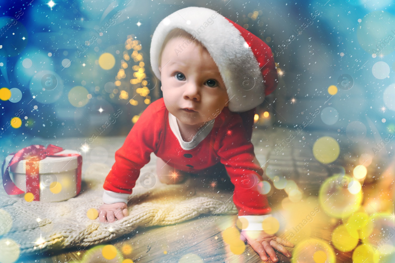 Image of Cute baby in Santa hat with Christmas gift on floor at home