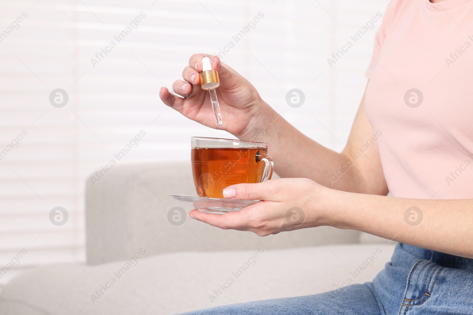 Photo of Woman dripping food supplement into cup of tea indoors, closeup. Space for text