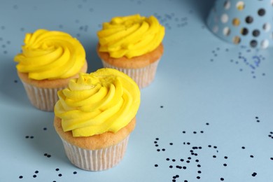 Photo of Delicious cupcakes with bright cream and confetti on light blue background, closeup. Space for text