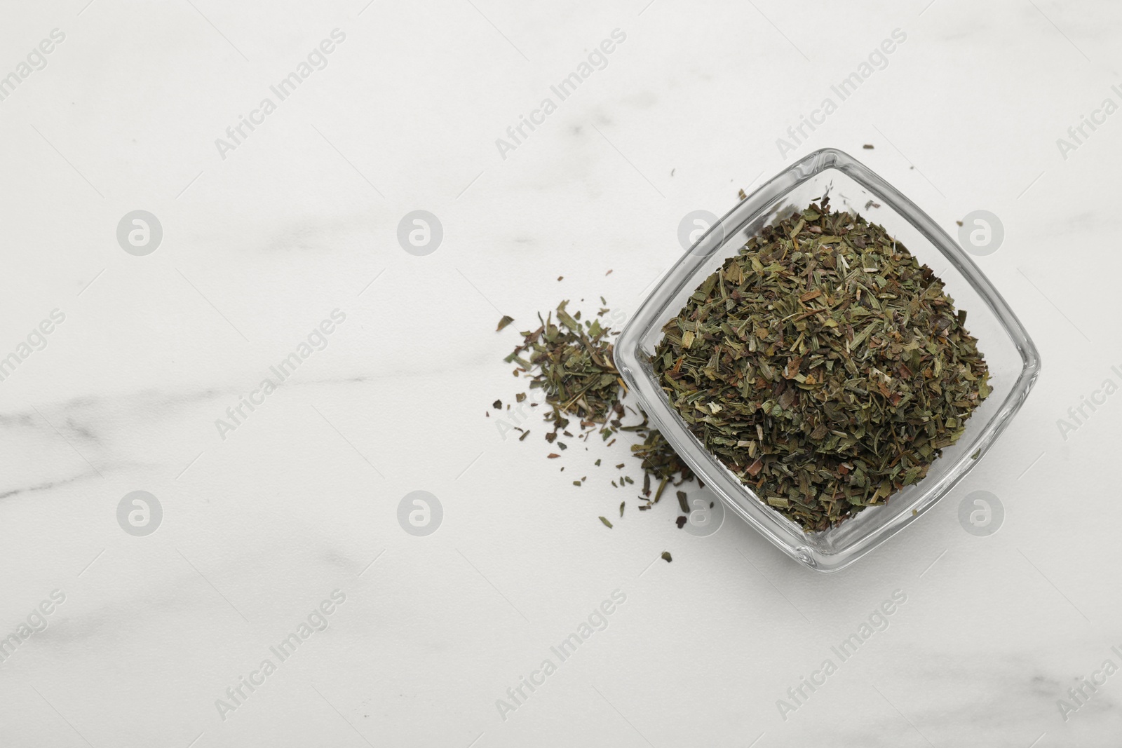 Photo of Dry tarragon in glass bowl on white table, top view. Space for text