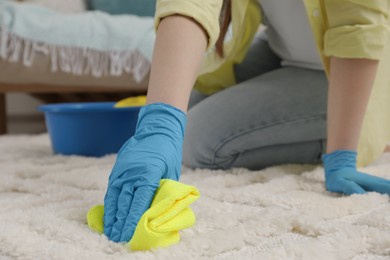 Photo of Woman in rubber gloves cleaning carpet with rag indoors, closeup. Space for text