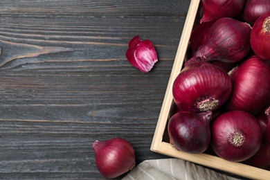 Photo of Crate with whole red onion bulbs and space for text on dark wooden background, flat lay