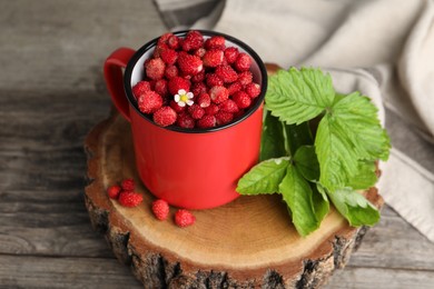 Fresh wild strawberries in mug and leaves on wooden table