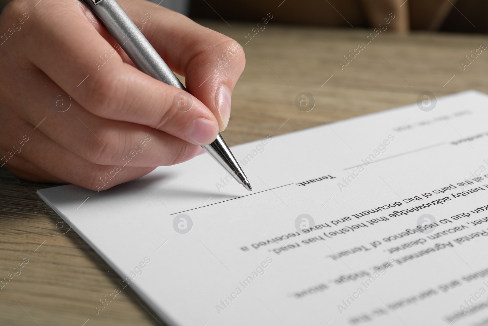 Photo of Woman signing document with pen at wooden table, closeup