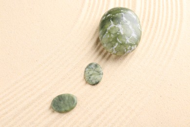 Photo of Zen garden stones on beige sand with pattern, flat lay