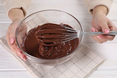 Photo of Woman mixing delicious chocolate cream with whisk at white wooden table, closeup