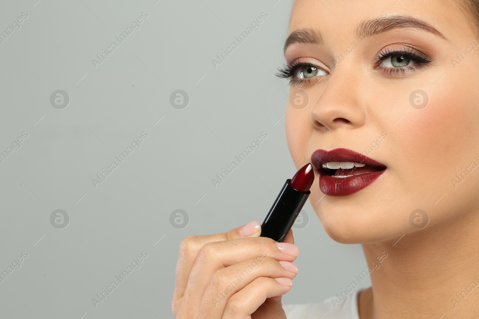Photo of Beautiful woman applying dark lipstick on gray background. Space for text