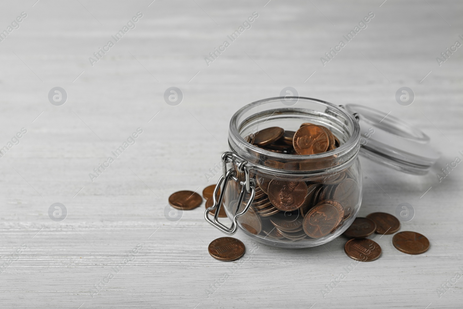 Photo of Glass jar with coins on white wooden table, space for text