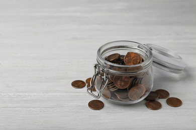 Photo of Glass jar with coins on white wooden table, space for text