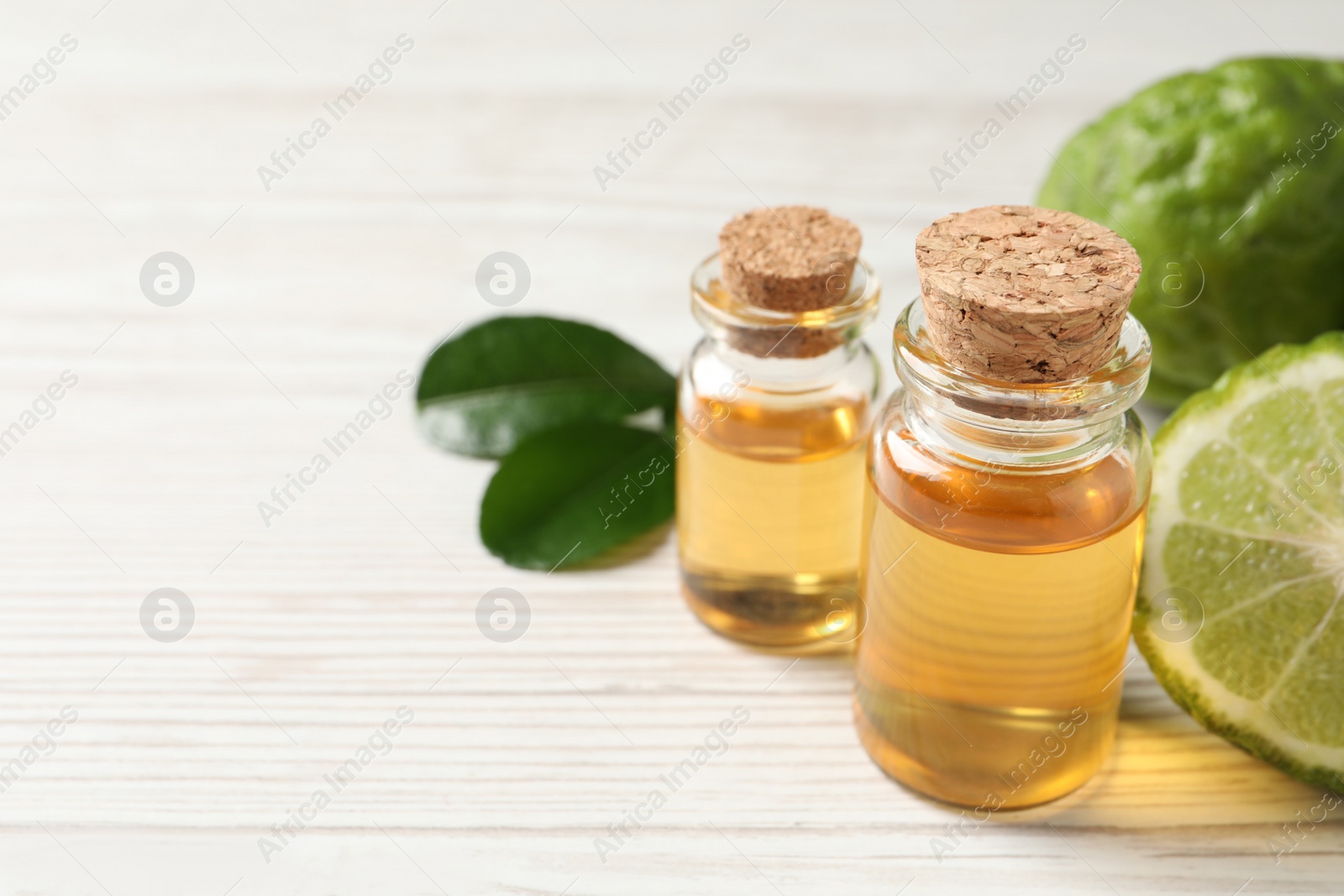 Photo of Glass bottles of bergamot essential oil on white wooden table, closeup. Space for text