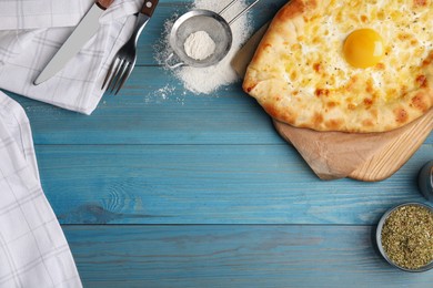 Fresh homemade khachapuri with cheese and egg served on light blue wooden table, flat lay. Space for text