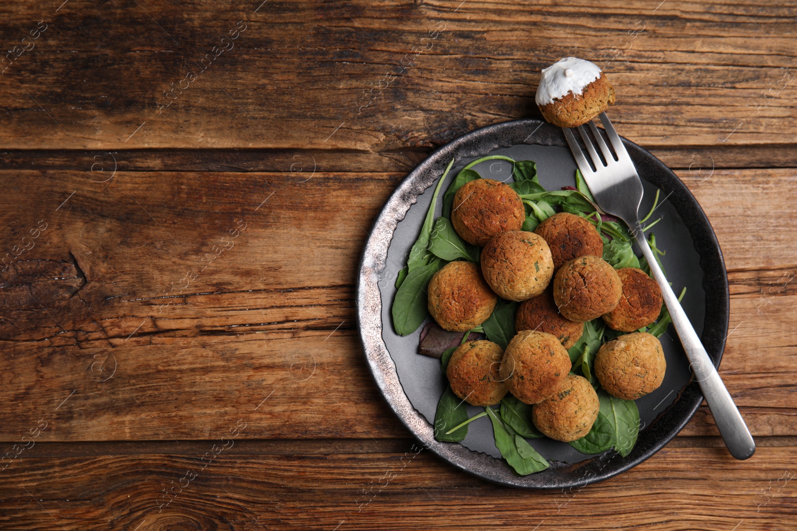 Photo of Delicious falafel balls with spinach and sauce on wooden table, top view. Space for text