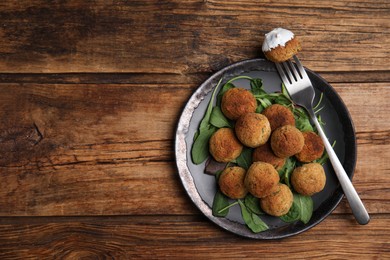 Delicious falafel balls with spinach and sauce on wooden table, top view. Space for text