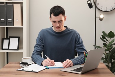 Photo of Man taking notes at wooden table in office