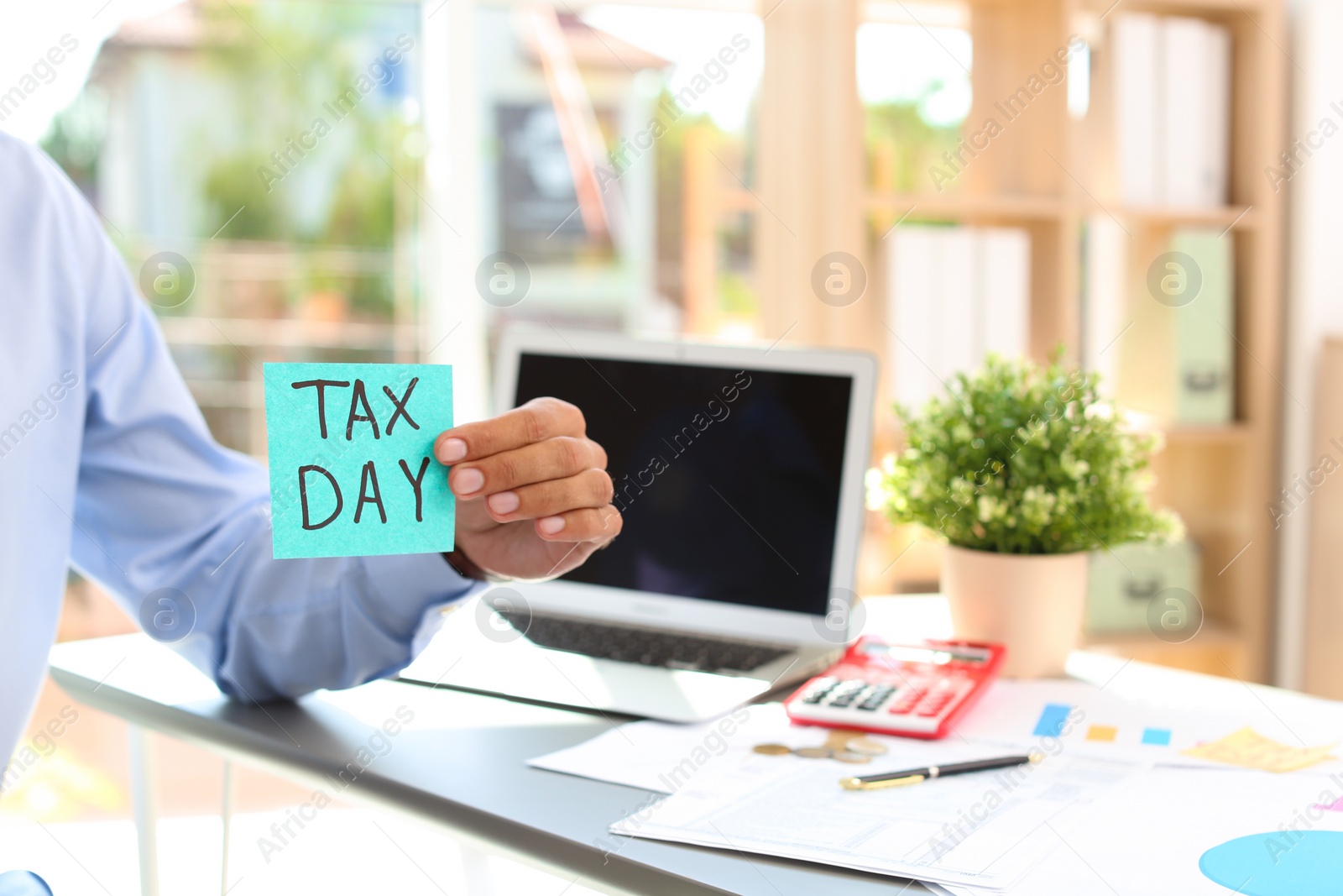 Photo of Man holding card with words TAX DAY indoors