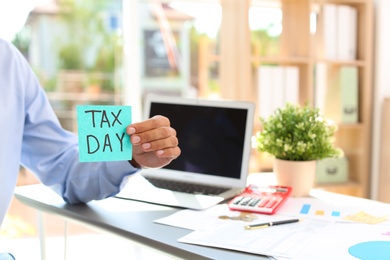 Photo of Man holding card with words TAX DAY indoors