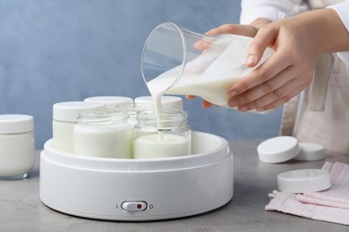 Photo of Woman pouring milk into glass jar at grey table, closeup. Making yogurt