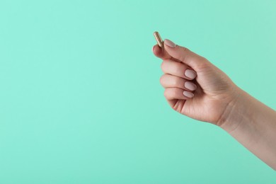 Photo of Woman holding vitamin capsule on turquoise background, closeup with space for text. Health supplement