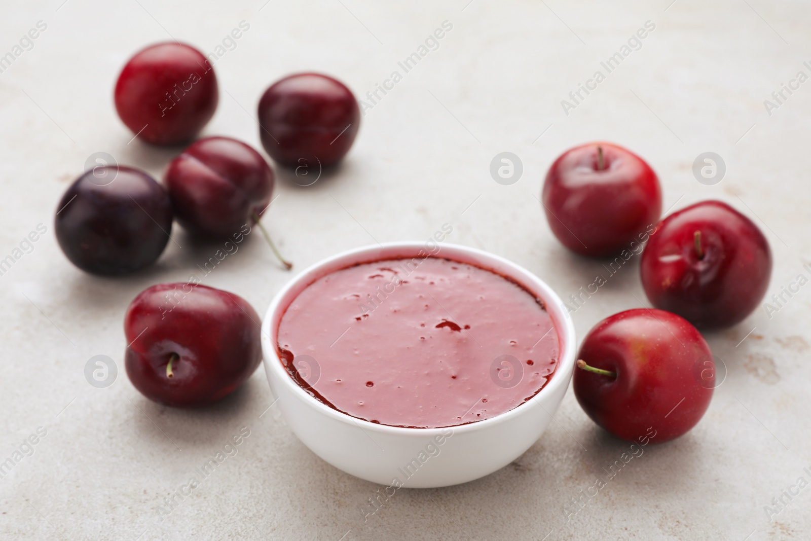 Photo of Plum puree in bowl and fresh fruits on light grey table