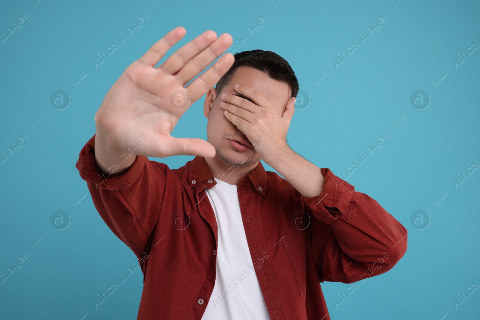 Photo of Embarrassed man covering face with hand on light blue background