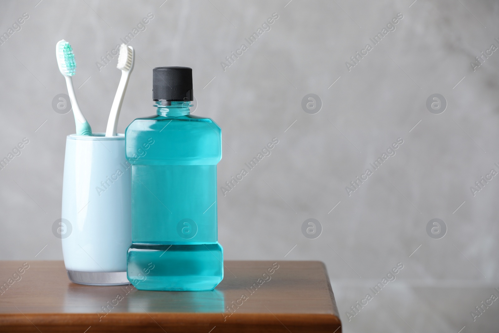 Photo of Bottle of mouthwash and toothbrushes on wooden table, space for text