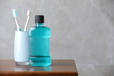 Photo of Bottle of mouthwash and toothbrushes on wooden table, space for text