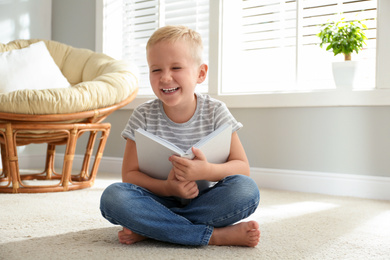 Cute little boy reading book on floor at home