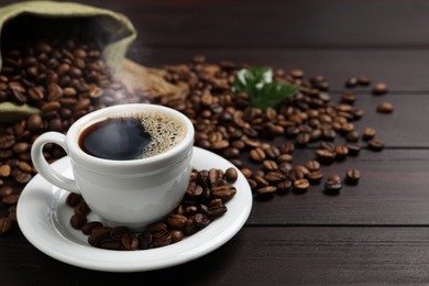 Cup of aromatic coffee and beans on wooden table. Space for text