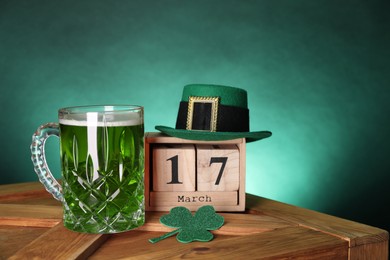 Photo of St. Patrick's day celebrating on March 17. Green beer, block calendar, leprechaun hat and decorative clover leaf on wooden table. Space for text