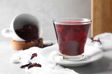 Aromatic hibiscus tea in glass, dried roselle calyces and sugar cubes on light table, closeup and space for text