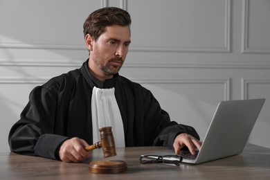 Judge with gavel and laptop sitting at wooden table indoors