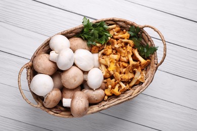 Basket with different mushrooms on white wooden table, top view