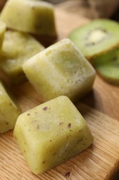 Photo of Frozen kiwi puree cubes and ingredient on wooden board, closeup