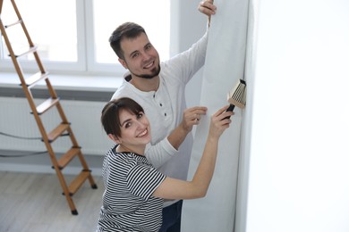 Photo of Woman and man hanging wallpaper in room