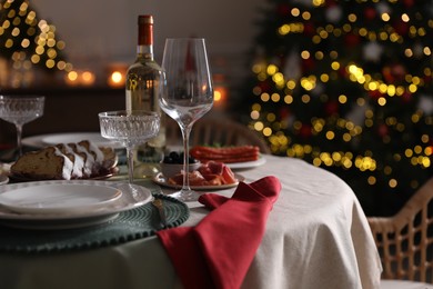 Photo of Christmas table setting with bottle of wine, appetizers and dishware indoors