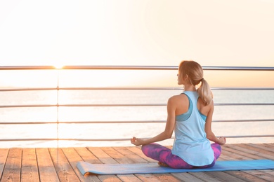 Photo of Young woman doing yoga exercises on pier in morning
