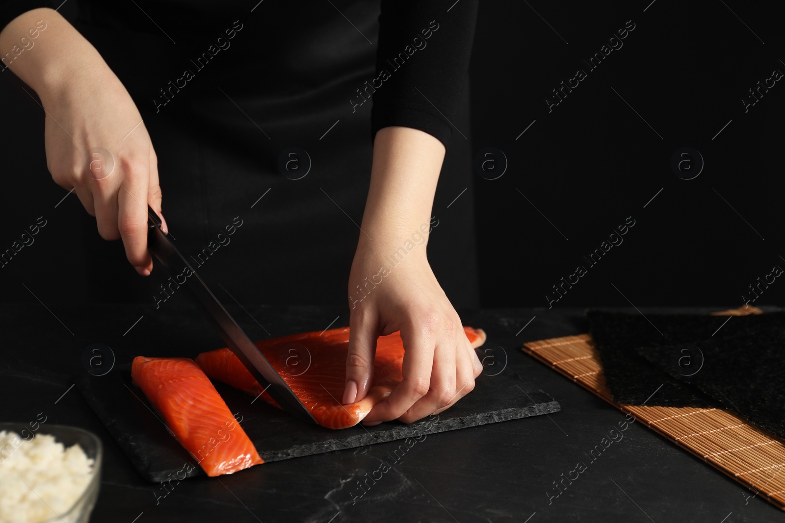 Photo of Chef cutting salmon for sushi at dark textured table, closeup