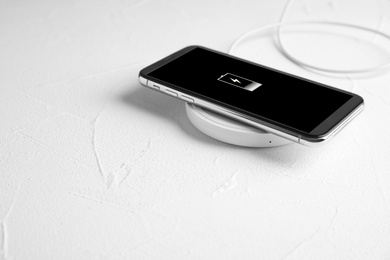 Photo of Mobile phone charging with wireless pad on white stone table. Space for text