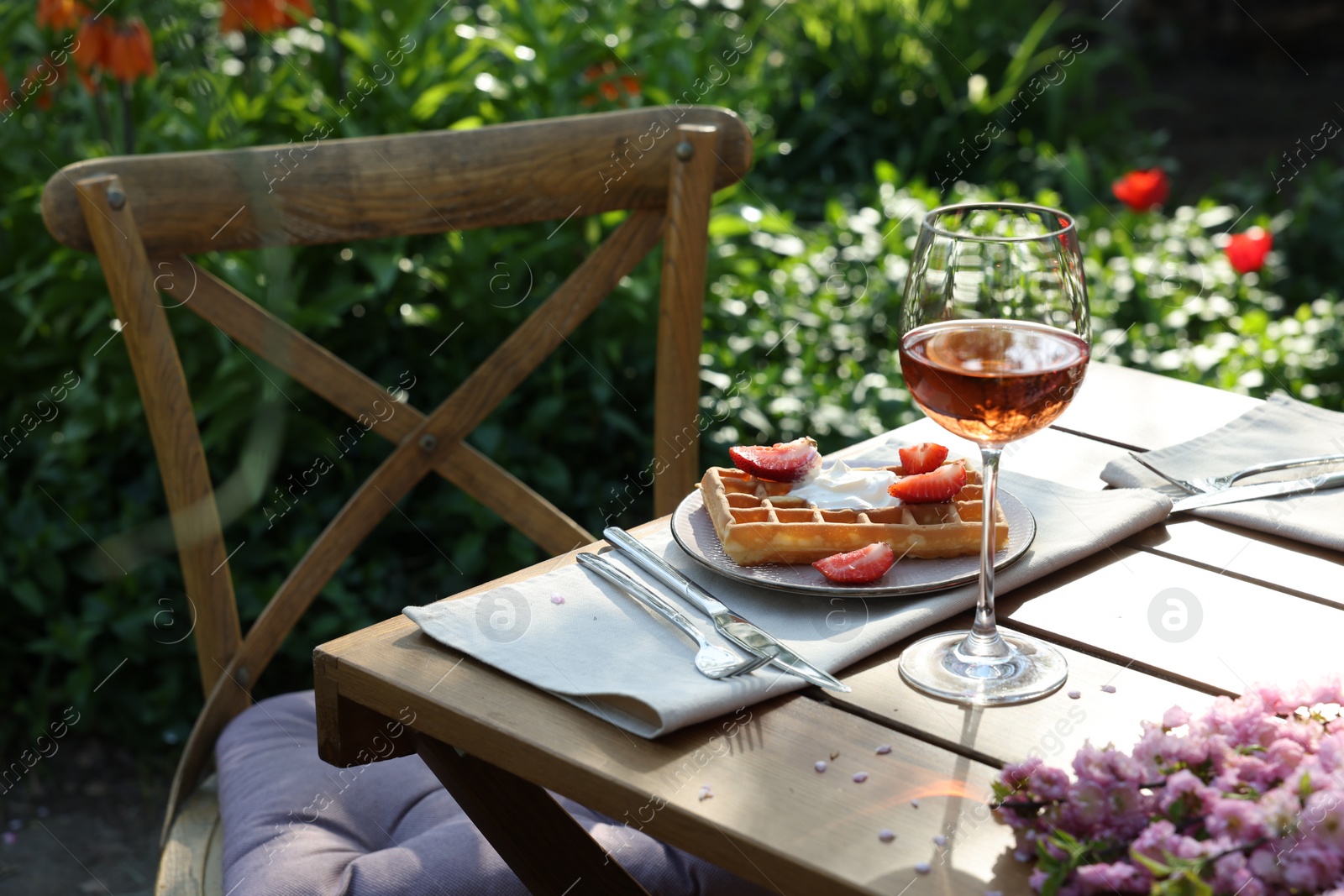 Photo of Delicious Belgian waffle with fresh strawberries and wine served on table in spring garden