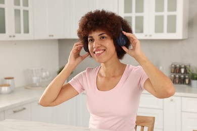 Beautiful young woman with headphones enjoying music at table in kitchen