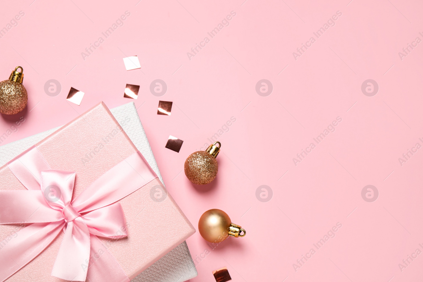 Photo of Beautiful gift boxes, golden Christmas balls and confetti on pink background, flat lay. Space for text