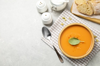 Photo of Tasty creamy pumpkin soup with basil in bowl on grey table, flat lay. Space for text