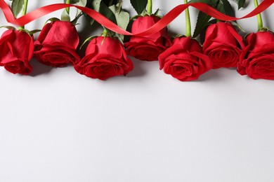 Beautiful red roses and ribbon on white background, above view. Space for text