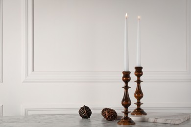 Photo of Elegant candlesticks with burning candles on white marble table. Space for text
